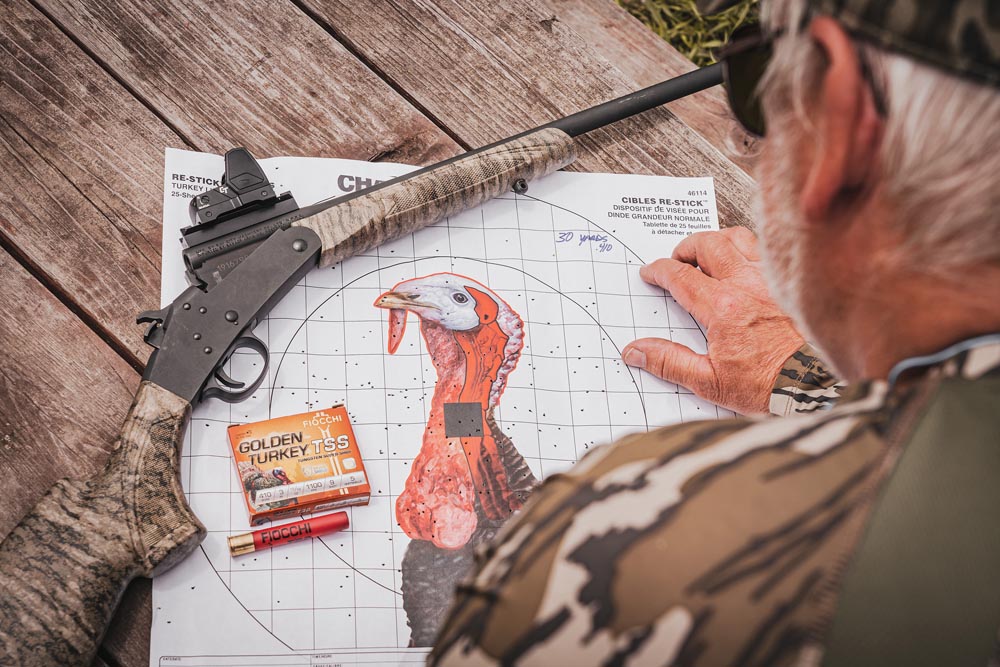 Savage_MinnesotaTurkeyHunt_051922-112_ds-Savage-Arms a man looking at a gun on a paper with a turkey picture